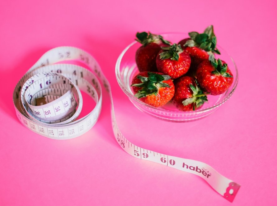 A glass bowl of fresh strawberries paired with a pink measuring tape symbolizes healthy eating.