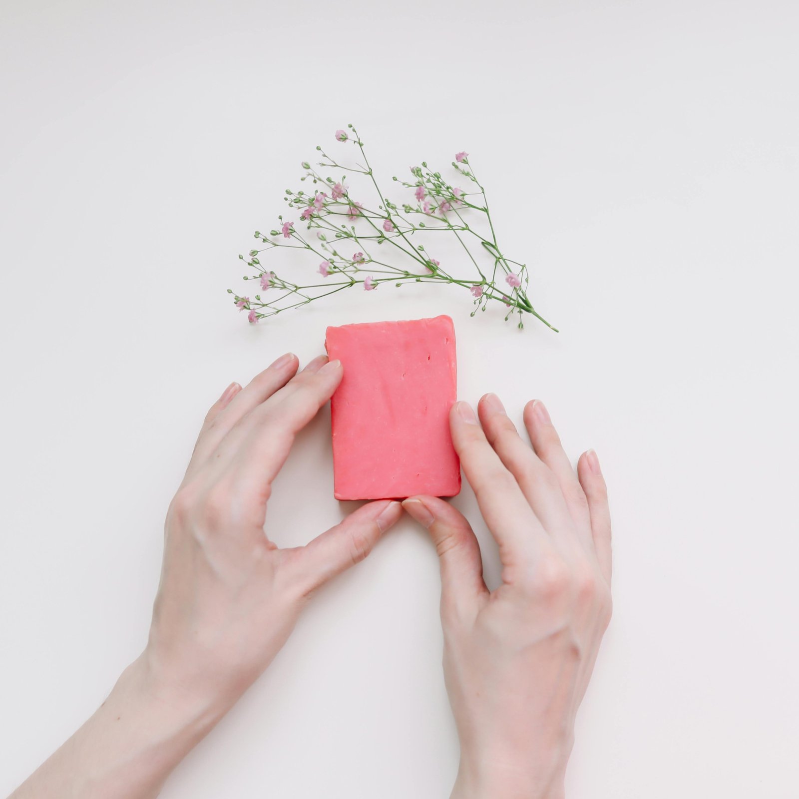 Hands holding a pink soap bar with white flowers on a clean background.