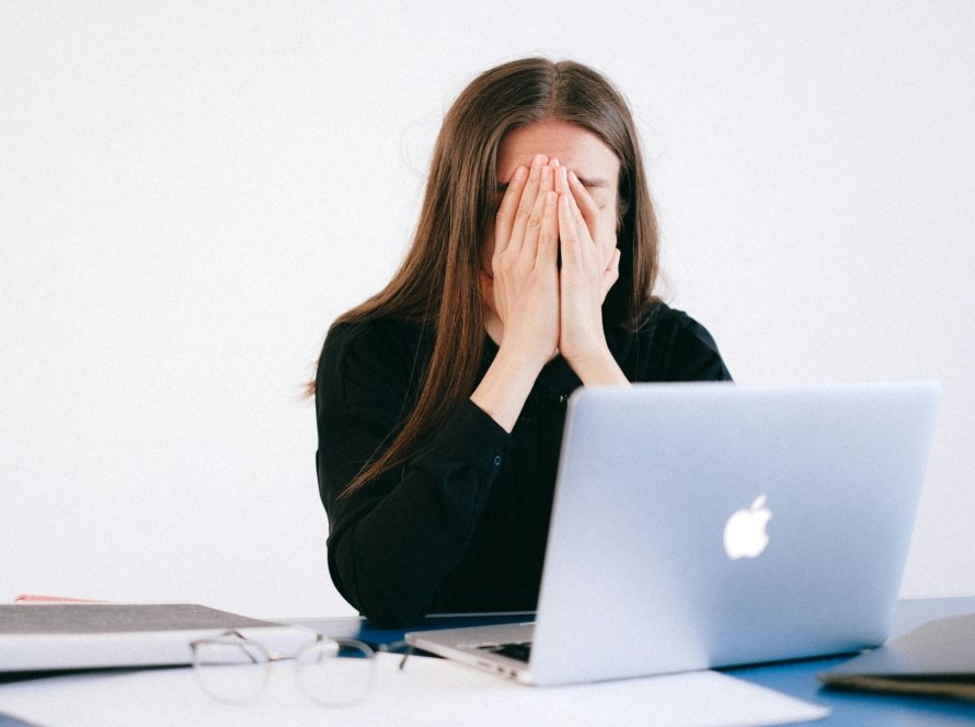 Woman feeling stressed and overwhelmed at her desk while working remotely on a laptop.