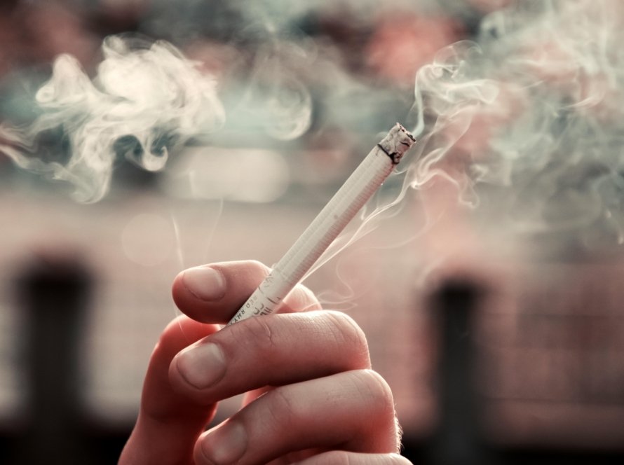 A close-up view of a hand holding a lit cigarette, with smoke visible in the air.