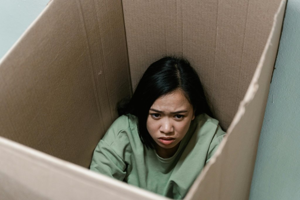 A woman inside a cardboard box symbolizes feelings of anxiety and claustrophobia.
