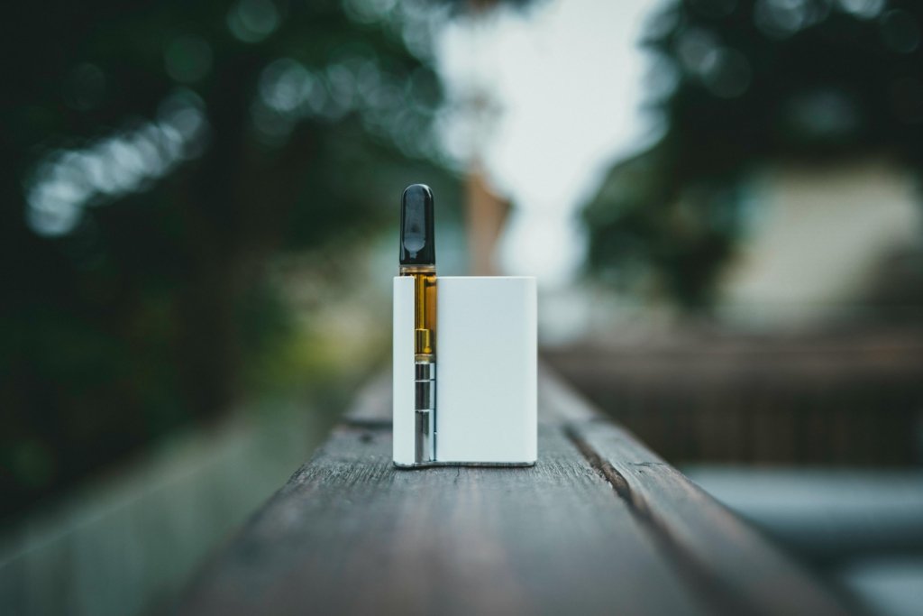 A sleek vape device resting on a wooden surface outdoors in natural light.